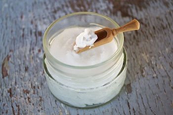 Coconut Oil Uses For Dogs - Coconut oil in a glass jar with a wooden spoon.