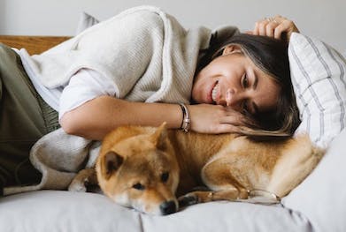 A woman and a dog lying on a sofa together. The woman is comforting the dog.